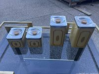 Three retro metal kitchen canisters of varying sizes with clear plastic lids and wooden knobs, in beige and brown vintage design.