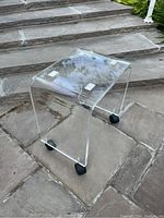 Lucite stool outdoors on stone steps showing full side profile and caster wheels.