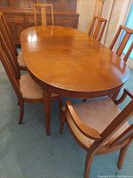 Oval solid wood dining table with six matching dining chairs upholstered in light beige fabric with floral pattern