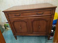 Solid wood buffet cabinet positioned against wallpapered wall, showing front view with drawer and doors closed.