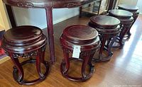 Five carved wooden stools arranged in a row beside a table, showing overall shape and condition.