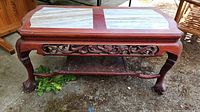 Front angled view of wooden coffee table with marble top panels and carved legs.