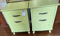 Front view of two yellow painted wooden end tables, showing drawer fronts and carved floral designs