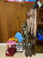 Photo showing all footwear, umbrellas, scarves, gloves, toque, and raincoats arranged on floor with wooden wall background.