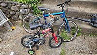 Two kids bikes outside with visible flat tires and training wheels on smaller bike