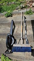 Full view of the Remington electric leaf blower beside push broom with blue bristles and car broom with metal handle.
