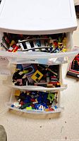 Three plastic drawers filled with assorted loose Lego bricks and parts including plates, slopes, wheels, minifigure pieces, track elements, and decorative tiles.