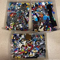 Three clear plastic bins filled with assorted Lego pieces in many colors and shapes, along with a Lego Ninjago flyer