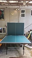 Full view of folded ping pong table upright with top half folded for playback practice, green playing surface with white lines.