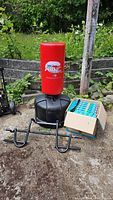 Wave Master punching bag with base, chin up bar, and box of foam pieces all displayed outdoors on concrete surface.