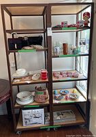 Two tall brown metal framed wooden shelf units on caster wheels. Shelves contain miscellaneous household and decorative items. Units show signs of wear and scuffs.