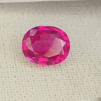 Close-up of the oval faceted hot pink sapphire or ruby gemstone on a white cloth background showing its color and cut details.