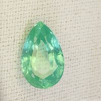 Close-up photo of green pear-shaped sapphire gemstone showing facets and color.