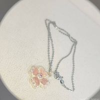 Photo showing the white gold chain with flower pendant featuring pink enamel petals and stones.