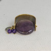 Front view of the amethyst swivel ring showing the large round polished amethyst stone, bead charms, and coin charm.