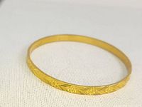 Gold-toned circular bracelet with detailed floral engravings visible against a neutral fabric background.
