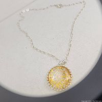 Front view of Avon necklace pendant showing yellow ornate design under clear faceted glass and silver-tone chain.