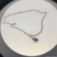 Close-up of the silver necklace with amethyst pendant showing deep purple gemstone and chain details.