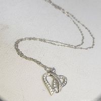 Heart pendant necklace with two interlocking hearts, one decorated with rhinestones and the other plain silver-tone metal, shown on white background to highlight detail