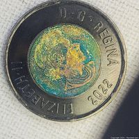 Close-up photo of the obverse side of the 2022 Canadian toonie showing the portrait of Queen Elizabeth II with distinct green and gold discoloration on the inner core due to plating flaw.