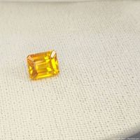 Close-up front view of the orange sapphire gemstone showing its emerald cut and bright orange color.