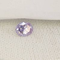 Pinkish purple oval cut tourmaline gemstone on a fabric background, showing facets and color.