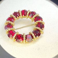 Top view of vintage red circular brooch with deep red rhinestones and gold twisted rope metal detail.