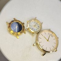 Three gold-tone watch heads arranged on a fabric surface showing dial faces and details.