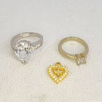 Photo of two rings and one heart pendant on white fabric background.