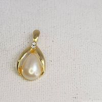 Front view of pendant showing teardrop-shaped faux pearl centerpiece framed in gold-tone metal with two small rhinestones near the bail.