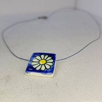 Front close-up of the square glazed porcelain pendant necklace showing white daisy flower on blue background.