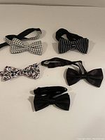 Five men's bow ties displayed on a white surface showing various colors and patterns.