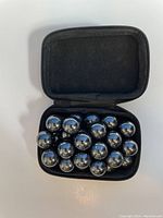 Open black zippered case containing 18 reflective metallic steel balls arranged in a single layer.