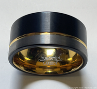 Close-up photo of men’s tungsten carbide ring showing the brushed black outer surface with a central gold band and the polished gold-tone interior stamped 'TUNGSTEN CARBIDE'.