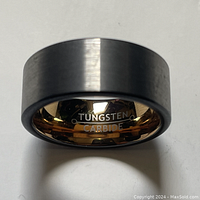 Front angle showing the polished gold-tone interior engraving 'TUNGSTEN CARBIDE' and brushed exterior surface of the ring.