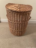 Front view of closed oval wicker basket with woven lid and side handles visible.