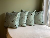 Four square green throw pillows arranged side by side showing brown diamond stitched pattern with knotted accents at intersections.
