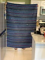 Full view of the rectangular area rug held vertically in a kitchen setting, showing the full dot pattern and size.
