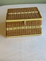 Closed wicker sewing basket on plain background showing woven pattern with yellow highlights and latch
