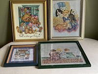 All four framed needlepoint artworks arranged on a white surface showing various scenes of teddy bears, children, animals, and text.