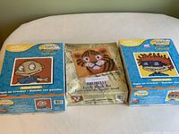 Three latch hook kits placed on a table: Rugrats Tommy on the left, vintage Terry Tiger in center, and Rugrats Chuckie on the right.