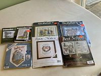 Nine packaged craft items including cross stitch kits and foam backings arranged on a surface