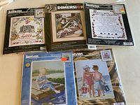 Five sealed cross stitch kits arranged flat showing various designs and packaging.
