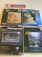 Photo shows the 4 cross stitch kits and the self-stick mounting board together as a collection, each kit still sealed in original packaging.