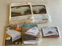 Photo of 5 packaged needlework fabric items with stamped patterns for cross stitch and embroidery, including Victorian lace lace-edged napkins and dresser scarfs in original packaging with pricing stickers.