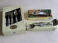 Set of Mikasa Arabella flatware and two spoon rests, in original boxes with decorative floral handles and vintage-style spoon rests.