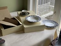 Full view of dinnerware pieces arranged on beige surface with boxes