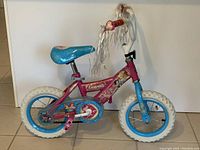 Side view of pink and blue princess-themed children's bicycle with white tires, chain guard, and adjustable seat.