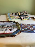 Bag of fabric quilting pieces with printed quilt blocks including snowmen patterns and village scenes, lying alongside a quilting calendar and instruction book.