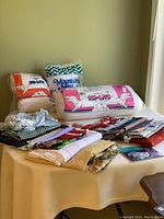 Photo showing assorted folded fabric, ribbons, and three large bags of quilt batting on a round table.